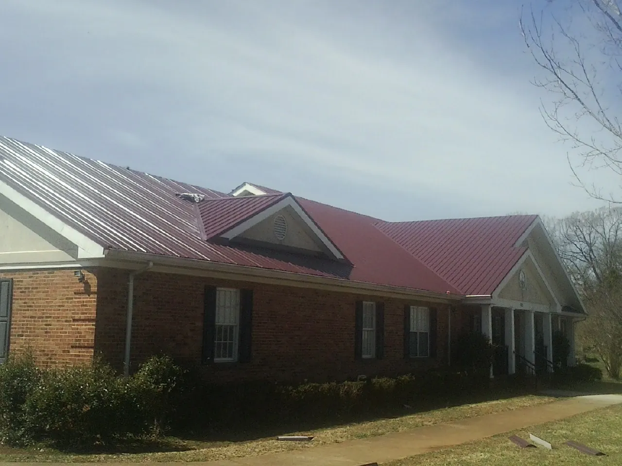 Red metal roof with gabled entries on a long brick building, from a Hail Damage Roof Repair job in West Sacramento