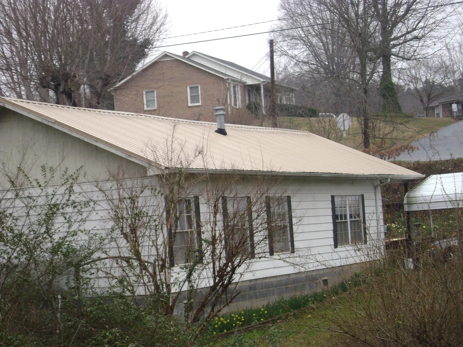 Tan metal roof on a white sided house set into a hillside — Commercial Roofing by Roofing Brothers in West Sacramento